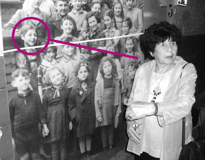 Irmgard Heimbach is standing in front of a large photograph showing a number of school children; a circle shows her face in the photograph.