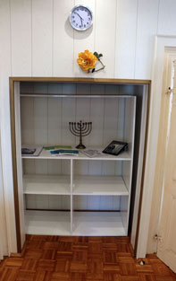 Cabinet in the wall with Hanukkah; above it, a flower and a clock.