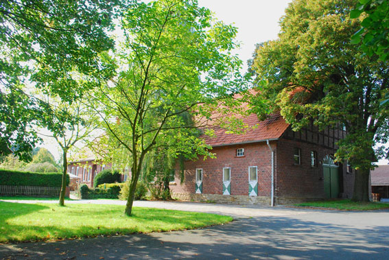 On the left, lawn with trees; on the right, exterior view of a brick building, single-storey but with a large pointed roof.
