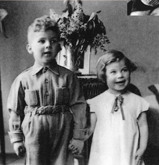 The children, standing next to each other and holding hands, are looking past the camera to the right; behind them is a vase.
